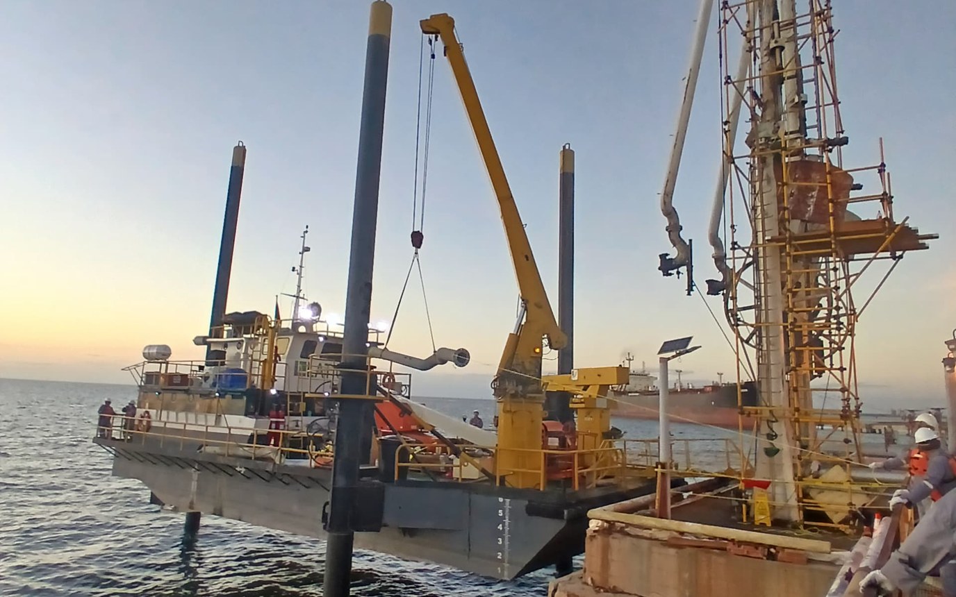 Unidad de LATICON en operación costa afuera en el Lago de Maracaibo, con las patas bajadas al fondo y la grúa de cubierta desplegada junto a una estructura de pozo, al atardecer